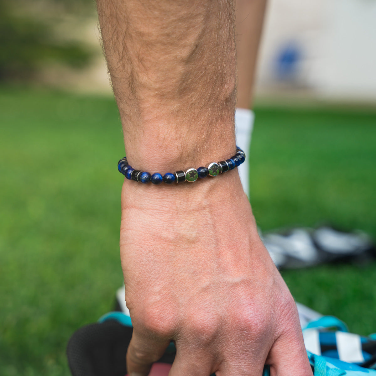 Bracciale artigianale da uomo indossato. Realizzato con occhio di tigre blu, agata nera e acciaio sul quale sono incise due stelle. Lab93Studio