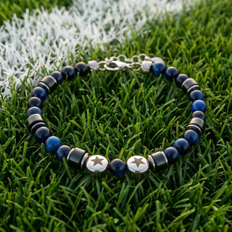 Bracciale artigianale da uomo su prato. Realizzato con occhio di tigre blu, agata nera e acciaio sul quale sono incise due stelle. Lab93Studio